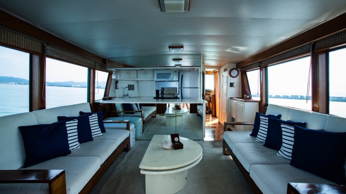 Salón interior de un yate clásico Hatteras 58 en Puerto Vallarta con sofás blancos, cojines azul marino a rayas y marcos de madera